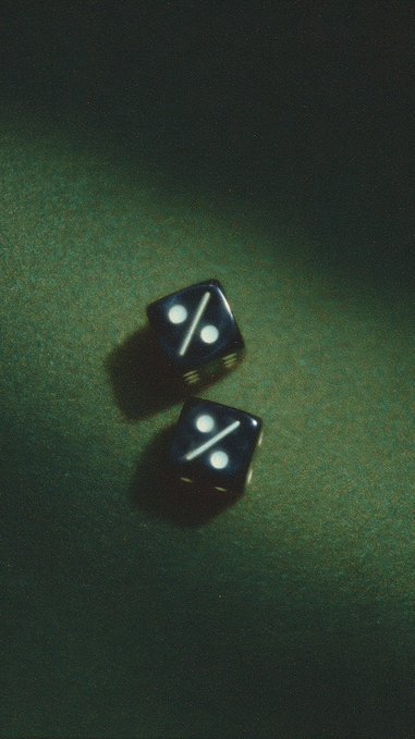 Moody, film-grain photograph of two black six-sided dice with white pips resting on a dark green textured surface.