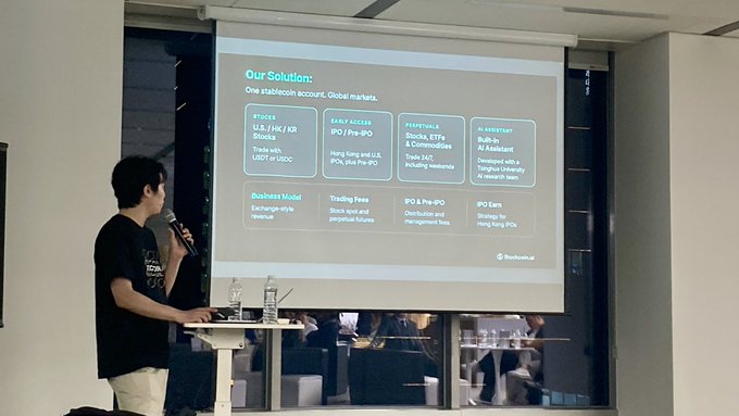 A presenter in a black t-shirt speaks into a microphone next to a projected slide titled 'Our Solution:' detailing a 'One Stablecoin account. Global markets.' business model for Blockrous.