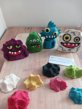 The image features a wooden table covered with various types of colorful playdough toys, including monster-shaped ones. The toys are arranged in different positions around the table, showcasing their unique designs and colors. A sign can be seen on the table that reads "10k awesome NFTs, 12k Twitter users, this is awesome, this is my work made with dough, hope you like it @gloobiez_eth". The post seems to be promoting a creative project involving playdough toys and possibly related to cryptocurrency or social media engagement.