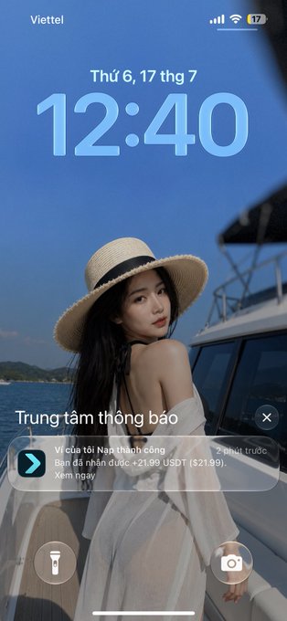 A smartphone lock screen showing the time '12:40' on 'Thứ 6, 17 thg 7' with carrier 'Viettel', featuring a woman in a straw hat on a boat and a notification in Vietnamese about a successful bank transfer of +21.99 USDT ($21.99).