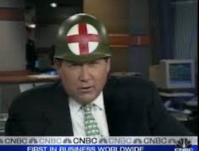 The image features a man wearing a red cross helmet with a white cross, sitting at his desk with an office chair behind him. There's also some computer equipment visible. The surrounding area suggests that he might be working for a company or organization with an interest in cryptocurrencies, such as Bitcoin.
