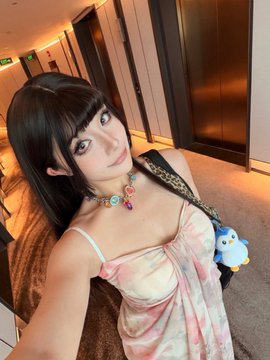 A dark-haired woman takes a selfie while holding up a small blue cartoon charm, likely from a game, smiling at the camera in a hotel hallway. The image ties to the post by visually backing up the claim that real women are genuinely into crypto gaming.