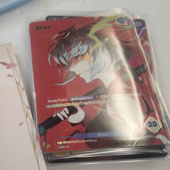 A stack of sealed trading cards featuring an anime-style character named "Shao" with a power level of 20, packaged in protective sleeves and labeled as card "ST1-02-001" illustrated by Arnold Tsang. The image shows a newly acquired "PR Shao" promo card from the Azuki TCG collection.
