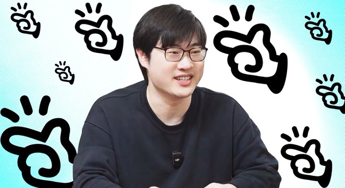 A smiling young man with glasses and a black sweater is photographed against a white background decorated with black cartoon hand/peace-sign icons.