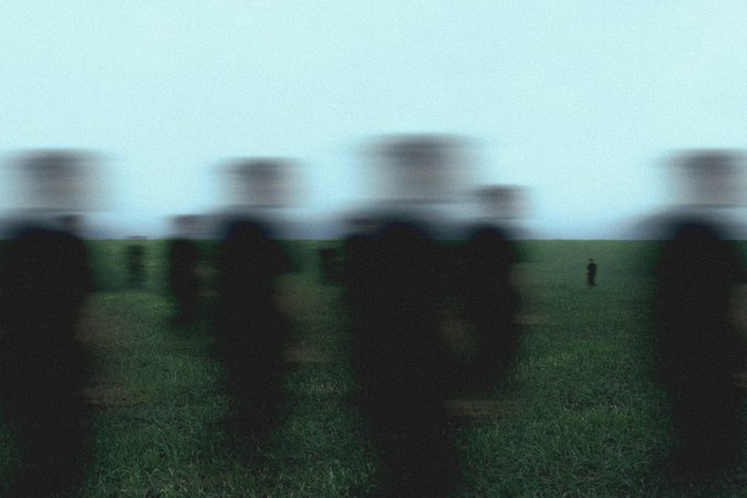 A blurry image shows dark, indistinct human silhouettes standing in a field of green grass under a pale blue sky, embodying the post's poetic theme of "silent shadows" drifting through the quiet earth. The figures appear as ghostly tremors between being and not being, matching the meditation on impermanence that accompanies the artwork's availability for 1.200Ξ on SR.