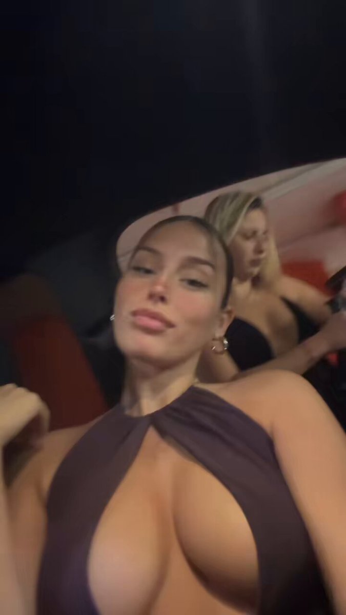 The image features a woman with large breasts wearing a tight-fitting dress, posing for a picture. The background of the photo shows two other women standing behind her, one of whom has their arm around another woman's shoulder. The caption on the image reads "More baddies = more invites #protocol #nolimit #solana $BTC $XLM". This suggests that there might be an event or gathering taking place where people are dressed up and interacting with each other, possibly related to a party or social occasion.