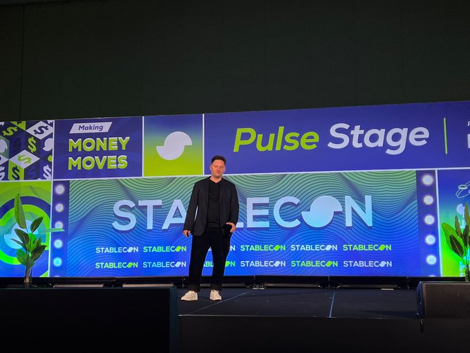 A man in a dark blazer stands on a stage in front of a large screen displaying 'Stablecon' branding and 'Pulse Stage' and 'Money Moves' sponsor logos.