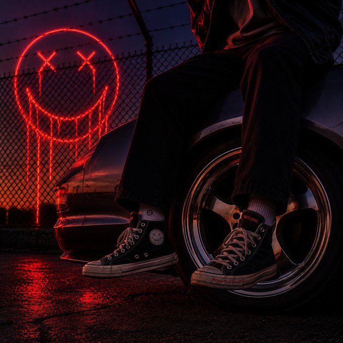 The image features a person sitting on a car tire, with their feet resting on the rim of the wheel. There are neon smiley faces painted on the fence behind them, adding a playful and quirky element to the scene. The caption "Normality is crowded average is already owned Be the outlier" suggests that this person's actions or appearance might be considered unusual or atypical in comparison to what is generally expected.