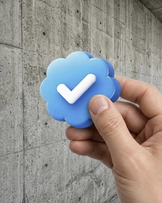 A hand holds a 3D blue cloud icon with a white checkmark against a gray concrete wall, resembling the iCloud verification symbol.