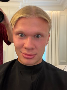 A blond young man with wide, startled blue eyes wears a black salon cape, with a "Before" caption suggesting a dramatic transformation was about to take place. The post's "After" portion contrasts with this initial wide-eyed, slightly frazzled look.