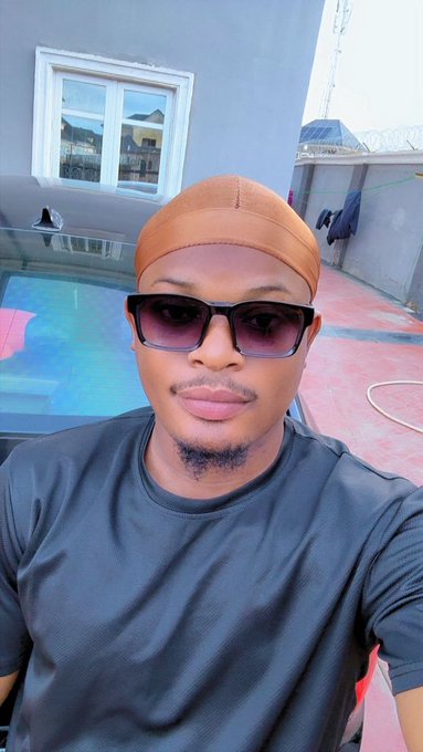 A young man wearing a tan durag, dark sunglasses, and a black t-shirt takes a selfie on what appears to be a rooftop terrace with a glass window and metal water tank in the background. The post humorously asks followers to drop their $TONCOIN address, jokingly claiming the photo reveals a long-lost family resemblance with his father.