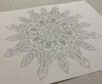 A pencil sketch of an intricate symmetrical mandala-like design featuring animal faces and leaves on white paper.