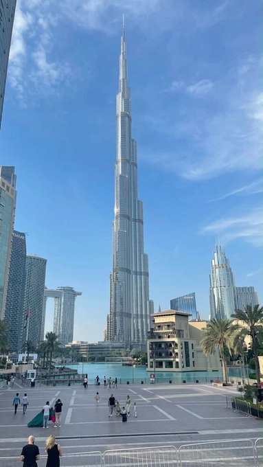 View of the Burj Khalifa towering over downtown Dubai with the Address Sky View and other skyscrapers under a blue sky, tourists walking in the plaza below.