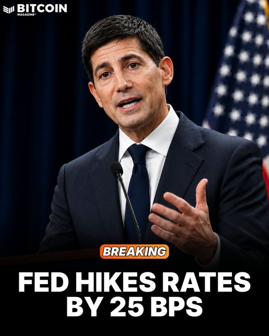 A man in a dark suit and tie speaks at a podium with an American flag in the background, with the Bitcoin Magazine logo in the top corner. The image is overlaid with bold text reading "BREAKING: FED HIKES RATES BY 25 BPS," directly reinforcing the accompanying post about the Federal Reserve's official 25 basis point interest rate hike announcement.