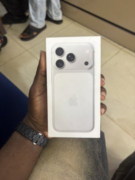 A hand holds up a newly purchased white iPhone box, likely the iPhone 17 Pro Max, with its distinctive triple-camera design visible on the packaging. The image captures a milestone moment of upgrading from the long-used iPhone 6 to a modern Apple device after a decade in the Web3 space.