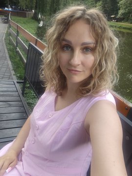 The image shows a woman with blonde hair sitting on a wooden bench next to a river, wearing a pink dress that complements her surroundings. She is smiling at the camera while waiting or taking a break from an event, such as soccer games. The photo also includes text in the caption stating "waiting for the world cup and even crypto can wait @Polymarket gives spain & france 16% each my heart already chose who are you rooting for?". This part of the image is likely meant to convey her excitement or enthusiasm towards a soccer event, as indicated by the caption.