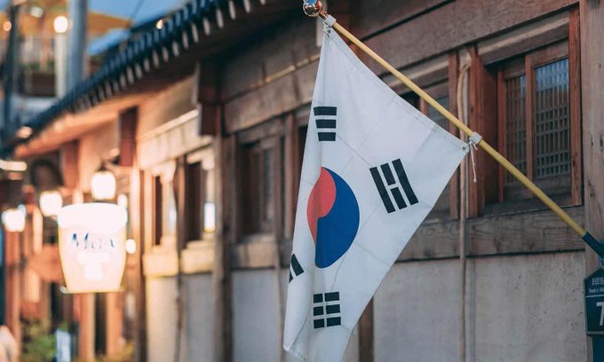The South Korean national flag hanging from a pole outside a traditional Korean hanok building at dusk.