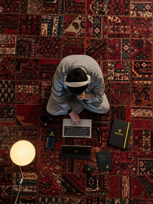 A man sits surrounded by Bynance-branded work materials—including a laptop, notebook, and merchandise—on a richly patterned red rug, embodying the post's message about embracing external cues to stay focused.