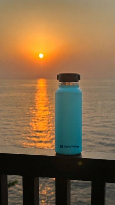 A turquoise Bitget Wallet water bottle sits on a railing against a stunning sunset over the ocean, symbolizing the start of a new journey with the right tools in hand.