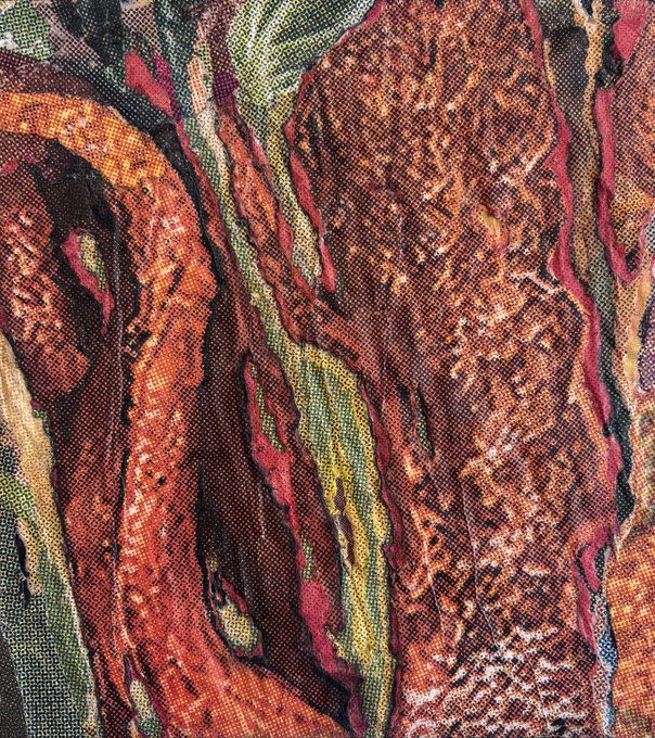 A close-up photograph of patterned fabric in warm tones of red, orange, brown, and green with a textured woven appearance.