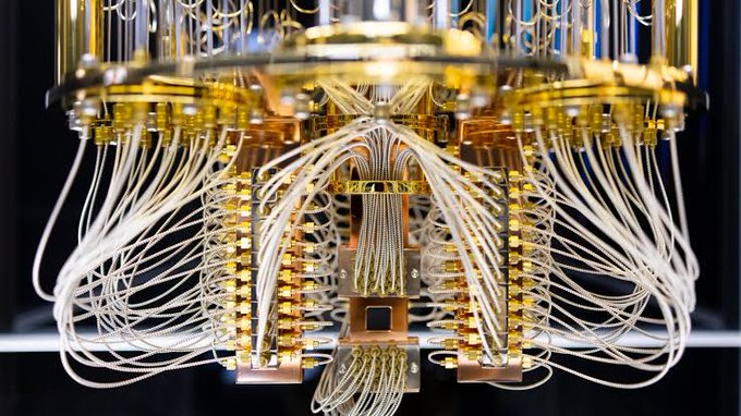 A close-up view of a quantum computer's dilution refrigerator, showing a cascade of gold-colored plates and numerous white cables.