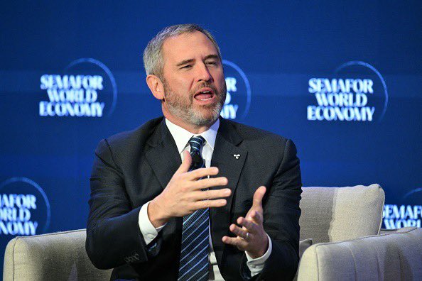 A man in a suit speaking and gesturing with his hands at a 'SEMAFOR WORLD ECONOMY' summit.