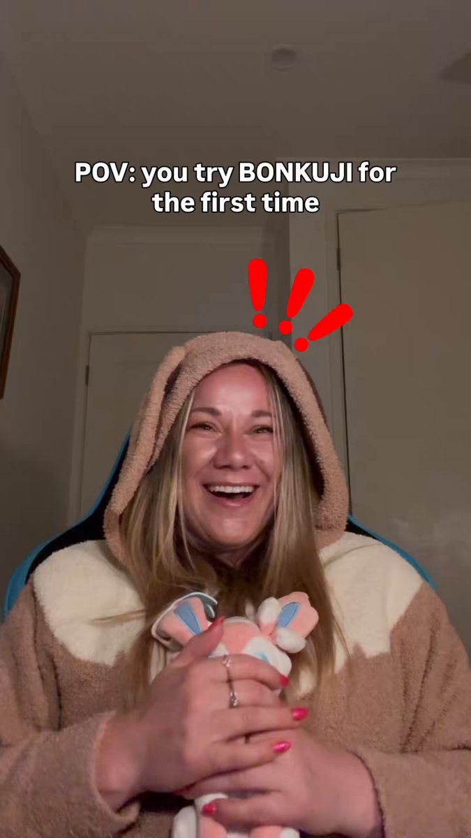 The image features a woman wearing a brown bunny costume, holding a stuffed animal. She has a big smile on her face as she looks directly at the camera. The caption of the image includes information about a new series called "BONKUJI" and mentions that it is an official TCG era release.