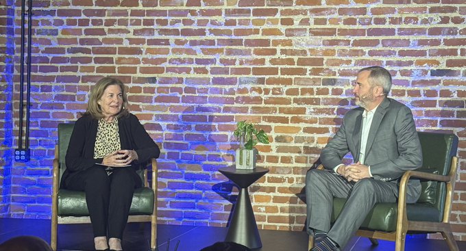 Two people, including Ripple CEO Brad Garlinghouse, sit on stage in chairs during a digital asset event in Kansas City, with a brick wall backdrop, sharing a conversation about crypto's future and the Clarity Act.