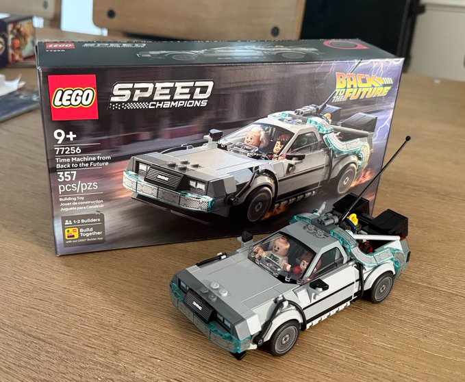 A LEGO Speed Champions set #77256 'Time Machine from Back to the Future' box displayed next to the assembled 357-piece DeLorean model on a wooden desk.