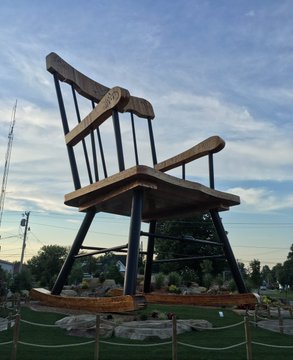 A massive wooden rocking chair sculpture displayed outdoors against a blue sky with scattered clouds.