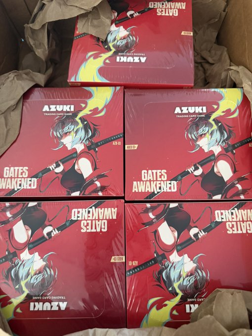 Multiple sealed boxes of the "AZUKI Trading Card Game: Gates Awakened" set are packed in a shipping carton, with visible "10 BX" and "A1K" labels indicating 10 booster boxes per case. The unboxing-style photo ties to the playful "Uh oh, where did this come from?" caption, suggesting a surprise shipment of Azuki TCG product arrived.