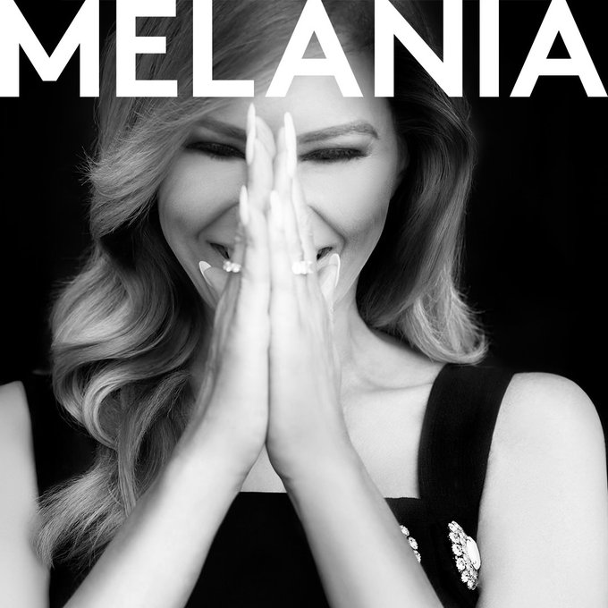 A black-and-white photo of Melania Trump smiling with her hands covering her face, with "MELANIA" displayed in bold white letters across the top. The image relates to the post by visually connecting to the surprise reaction over her releasing a new music project.