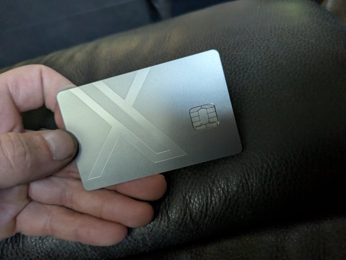 A hand holds a silver metal crypto card with a chip and geometric design against a dark leather background
