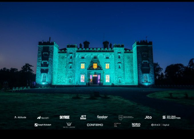 A castle illuminated with bright cyan lighting against a dark night sky, with sponsor logos including Altitude, SKYRISE, JET, Seeker, Jito, IRACE Digital, and NORIG displayed at the bottom.