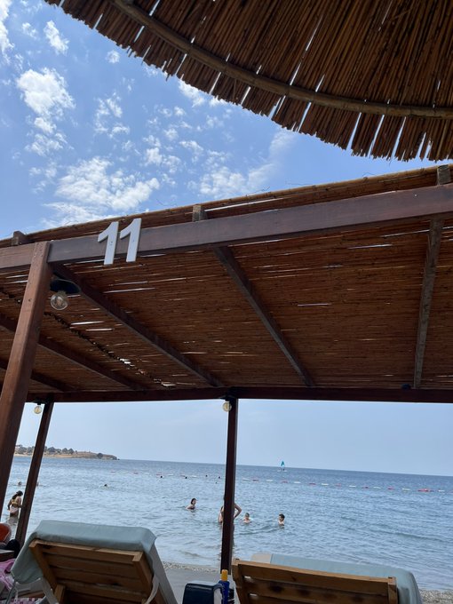 A beachside cabana marked "11" overlooks swimmers enjoying the sea, while a thatched umbrella in the foreground frames a relaxing coastal view. The scene captures a perfect weekend vibe, inviting followers to share their rest and fitness routines.
