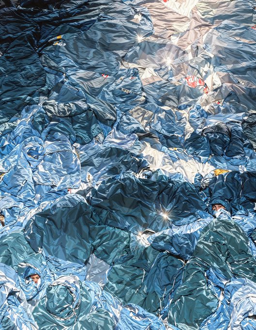 An artistic close-up of a crumpled blue tarp with reflective highlights creating a starburst effect across its wrinkled surface.