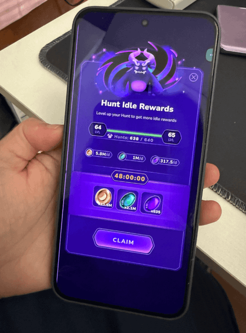 A hand holding a smartphone displaying a "Hunt Idle Rewards" screen from a game, showing level progression from 64 to 65 with a "CLAIM" button.