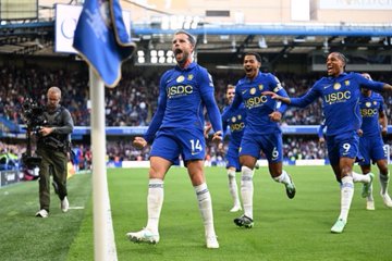 Leicester City soccer players in blue kits, with the number 14 visible on the jersey of a celebrating player in the foreground, run toward the corner flag during a match.