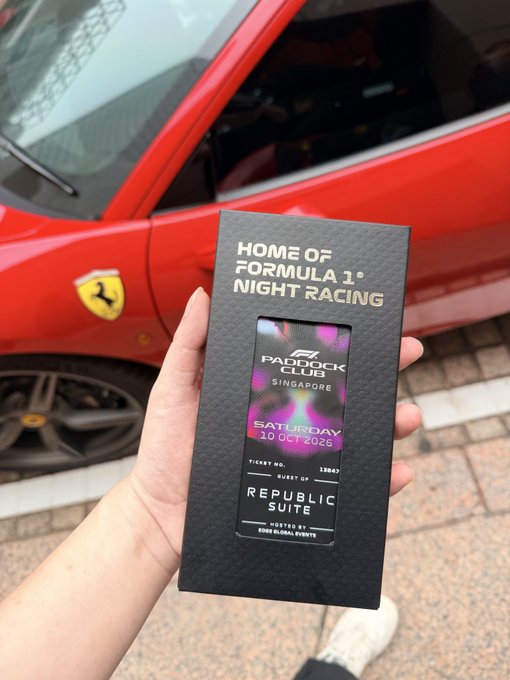 A hand holds an "F1 Paddock Club Singapore" ticket for Saturday, 18 Oct 2025, at the Republic Suite, in front of a red Ferrari with the iconic prancing horse emblem, perfectly matching the F1 racing experience and luxury car atmosphere.
