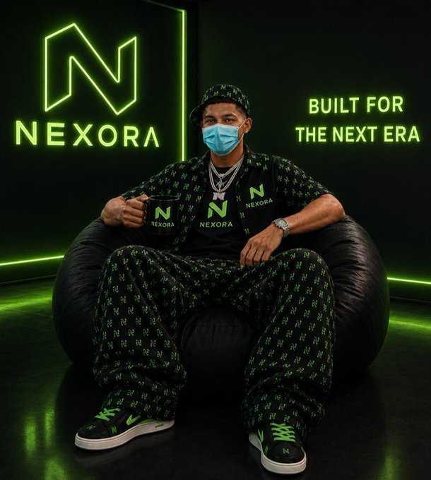 A man wearing a green 'NEXORA' branded cap, shirt, and pants sits in a beanbag chair, with a glowing green 'NEXORA' logo and the tagline 'BUILT FOR THE NEXT ERA' visible on the wall behind him.