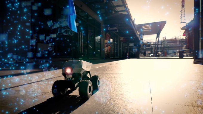 A small four-wheeled robot with a red light navigating an urban plaza at sunset, surrounded by floating blue particles.