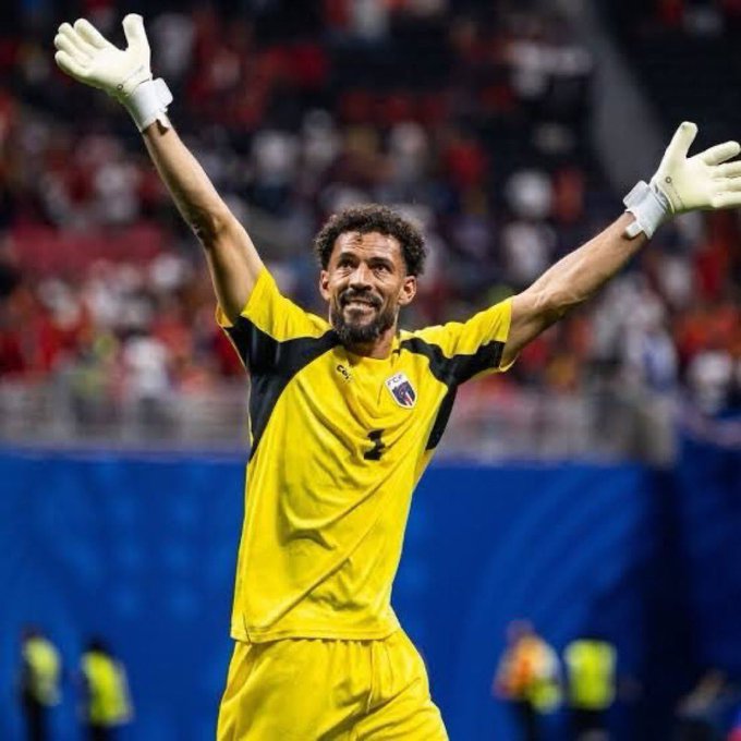 A bearded soccer goalkeeper wearing a bright yellow and black #1 jersey with white gloves stands triumphantly with both arms raised in celebration before a cheering crowd. His joyful, victorious pose embodies the post's message of perseverance, illustrating how not giving up can lead to a triumphant breakthrough.
