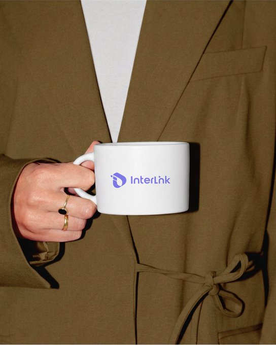 A person wearing a tan blazer holds a white mug featuring the "InterLink" logo in blue, visually tying into the GM morning greeting for the InterLink (ITLG/ITL) stock community.