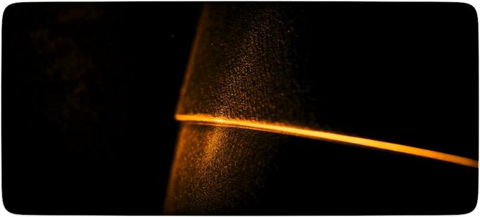 A dark, minimalist image shows a textured surface illuminated by a single, thin orange light line cutting across it.