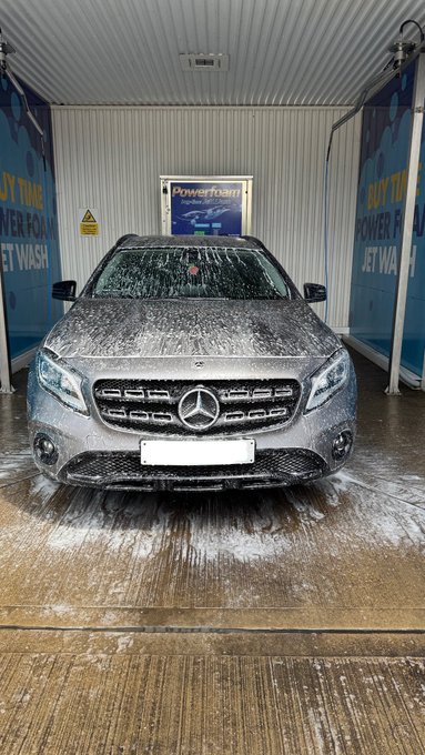 A Mercedes-Benz, likely an E-Class, is covered in foam inside an automated "Powerwash" car wash bay. The image's depiction of a clean, luxurious vehicle appears to be used as a visual metaphor by the poster, who is offering a coffee to their "GM family" (good morning family) and announcing a giveaway where they will pick a winner to drop SOL (Solana) crypto wallets to.