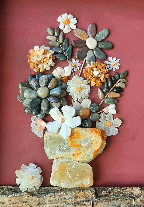 An artistic arrangement of polished stones, crystals, and carved stone flowers crafted into the shape of a floral bouquet, displayed against a maroon wall.