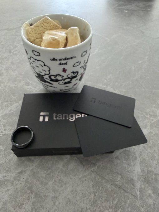 The image shows a white mug with cartoon clouds and the text "alle anderen: doei" filled with sugar cubes, alongside black "tangem" branded packaging and a card. The visual ties into the post's message about self-custody by showcasing Tangem, a hardware wallet product, reinforcing the importance of taking personal control of crypto assets amid tightening European regulations.