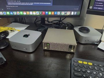 Three compact computers (two silver Mac Minis and one in a custom textured case) sitting on a desk next to a monitor and keyboard.