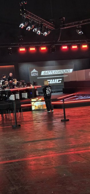 A person wearing a jersey with '67' walking on a stage in an arena setting with 'BATTLEGROUND' displayed on a large screen.
