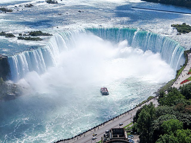 An aerial photograph of a massive horseshoe-shaped waterfall with a tour boat navigating the turbulent waters below, mist rising from the cascade.